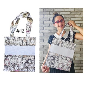 May include: A white tote bag with a black and white illustration of faces on the front. The bag has a white fabric insert with a white border. The bag has black handles and the number #12 is printed on the front of the bag.