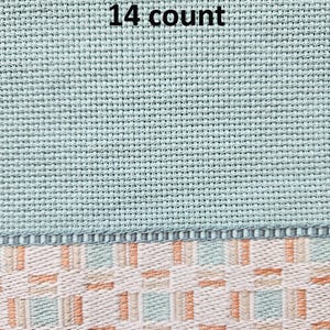 May include: Close-up of a section of cross-stitch fabric. The top portion is a light teal color with the text "14 count" in black. The bottom section features a woven pattern in white, peach, and teal.