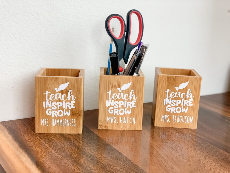 May include: Three wooden pencil holders with the text "teach inspire grow" and the names of three teachers: Mrs. Hammerness, Mrs. Hatch, and Mrs. Ferguson.