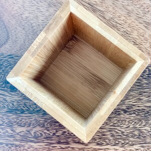 May include: A square wooden box with a natural wood finish. The box is empty and has a smooth, polished surface.