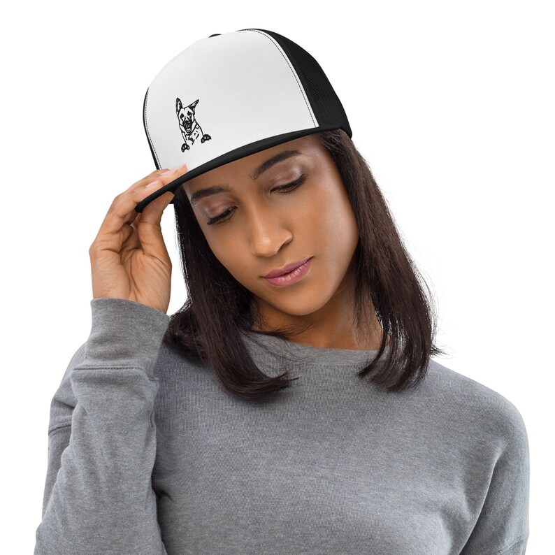 May include: A black and white illustration of a dog is embroidered on a white trucker hat with a black mesh back.