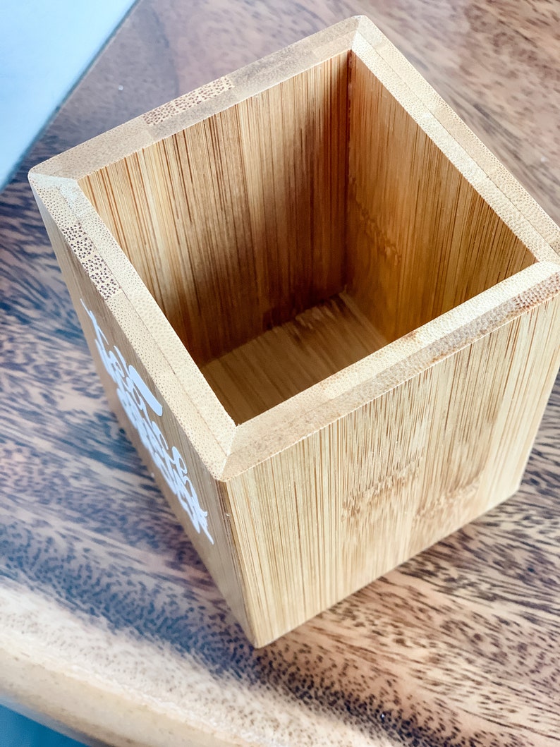 May include: A small, square, wooden container made of bamboo. The container is empty and has a light brown colour.