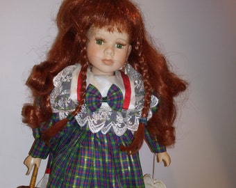 May include: A porcelain doll with red hair in braids, wearing a green, red, and blue plaid dress with a white lace trim and a red ribbon. She is holding a small wicker basket.