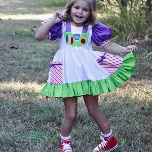 May include: A white dress with purple puff sleeves and a green hem, inspired by a space ranger. The dress features a green and white chest panel with a red and green design. The outfit is completed with red sneakers and white socks.