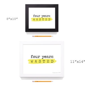 以下が含まれることがあります： 黄色い背景に黒い文字で「four years wasted」と書かれた額装されたプリントが2枚。小さい方のプリントは8インチ&times;10インチ、大きい方のプリントは11インチ&times;14インチです。