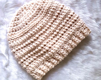May include: A cream-colored crocheted beanie hat. The hat is made with a textured stitch and has a slouchy fit.