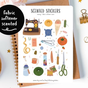 May include: A sheet of scented stickers with sewing-themed illustrations, including a sewing machine, scissors, needles, thread spools, and a pincushion. The text "SCENTED STICKERS" and "fabric softener scented" are visible. The stickers are on a spiral notebook.