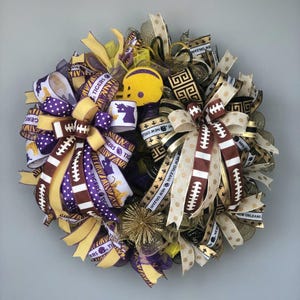 May include: A decorative wreath featuring football-themed ribbons in purple, gold, and brown. The wreath includes a small yellow football helmet and ribbons with the text "Tigers" and "New Orleans".