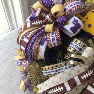 May include: A decorative wreath featuring football-themed ribbons in purple, gold, and brown. The ribbons display footballs, the word "Tigers", and the phrase "New Orleans". The wreath has a festive, celebratory appearance.