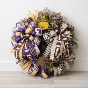 May include: A decorative wreath featuring football-themed ribbons in purple, gold, and brown. The wreath includes a miniature yellow football helmet and ribbons with the text "Tigers" and "New Orleans".