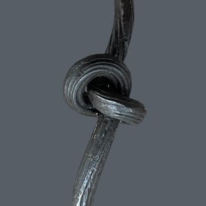 May include: A handcrafted, dark metal door handle with a unique knot design. The handle features a loop at the top and bottom, and the central knot adds a decorative element. The metal has a textured surface.