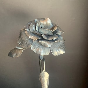 May include: A silver metal rose sculpture with a single leaf on the stem. The rose is made of many individual petals.