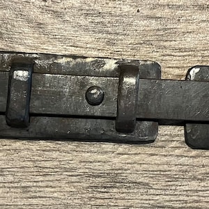 May include: Black metal door latch with a rounded handle and a rectangular plate. The latch is designed for use on doors, gates, or cabinets.