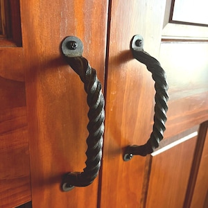 Może przedstawiać: Dwa czarne, skręcone metalowe uchwyty do drzwi są zamontowane na drewnianych drzwiach.