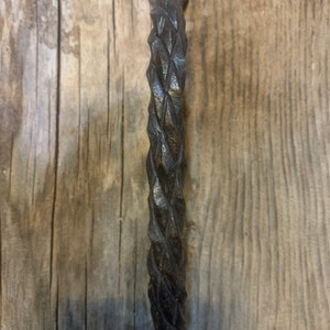 May include: A black metal door handle with a twisted, rope-like design. The handle is attached to a wooden surface.