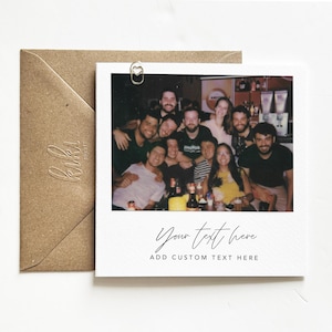 Puede incluir: Una impresi&oacute;n fotogr&aacute;fica cuadrada estilo polaroid con un grupo de personas sonriendo. La foto est&aacute; adherida a un fondo blanco con un clip de papel dorado en forma de coraz&oacute;n. Un sobre marr&oacute;n est&aacute; a la izquierda. El texto "Your text here" y "Add custom text here" est&aacute;n en la foto.