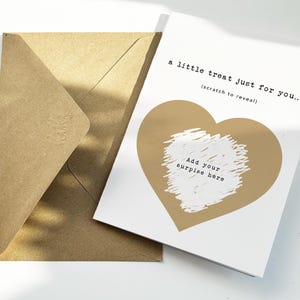 以下が含まれることがあります： 金色のハートのデザインと「a little treat just for you... (scratch to reveal)」の文字が入った白いカード。カードには「Add your surprise here」の文字も入っています。茶色の封筒がカードの隣にあります。