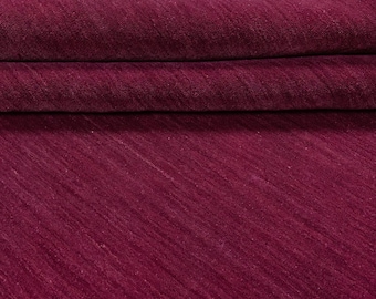 May include: A folded, deep burgundy rug with a textured surface. The rug's color is a rich, saturated shade of red-violet. The diagonal weave pattern is visible, adding depth and visual interest to the textile.