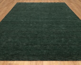 May include: A rectangular, dark green rug with a textured surface. The rug is placed on a light brown wooden floor, creating a contrast in color and texture. The rug appears to be made of a soft material.