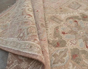 May include: A rolled-up rug with a detailed, traditional pattern in beige, tan, and muted red. The rug displays geometric and floral motifs. The edges are finished with a darker brown border, adding a touch of elegance.