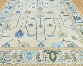 May include: A cream-colored rug with a traditional Persian design. The rug features a central medallion with intricate floral patterns in shades of blue, green, and beige. The border of the rug is also decorated with floral motifs.
