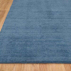 May include: A blue area rug with a textured surface. The rug is a solid color and appears to be made of a soft material. The rug is placed on a wooden floor.