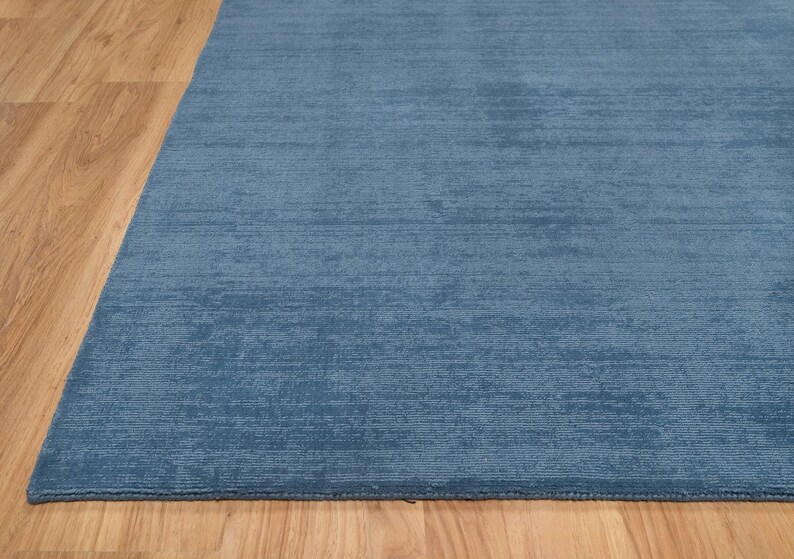 May include: A blue area rug with a textured surface. The rug is a solid color and appears to be made of a soft material. The rug is placed on a wooden floor.