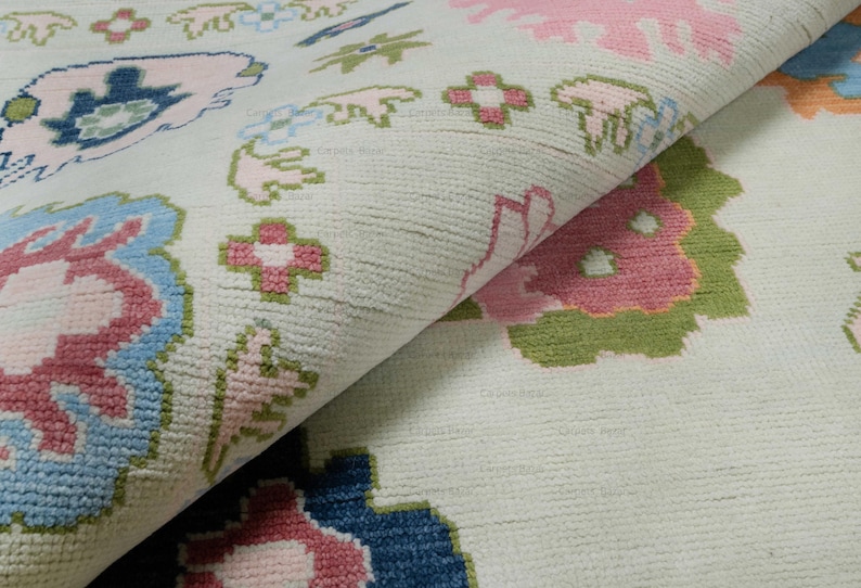 May include: Close-up of a white rug with a floral pattern in shades of pink, blue, and green. The rug has a soft, textured surface.
