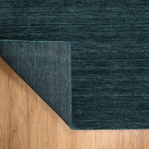 May include: A teal-colored rug with a textured surface. The corner of the rug is folded back, revealing the underside. The rug is placed on a wooden floor.
