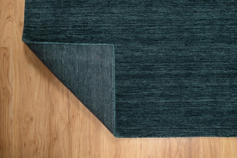May include: A teal-colored rug with a textured surface. The corner of the rug is folded back, revealing the underside. The rug is placed on a wooden floor.