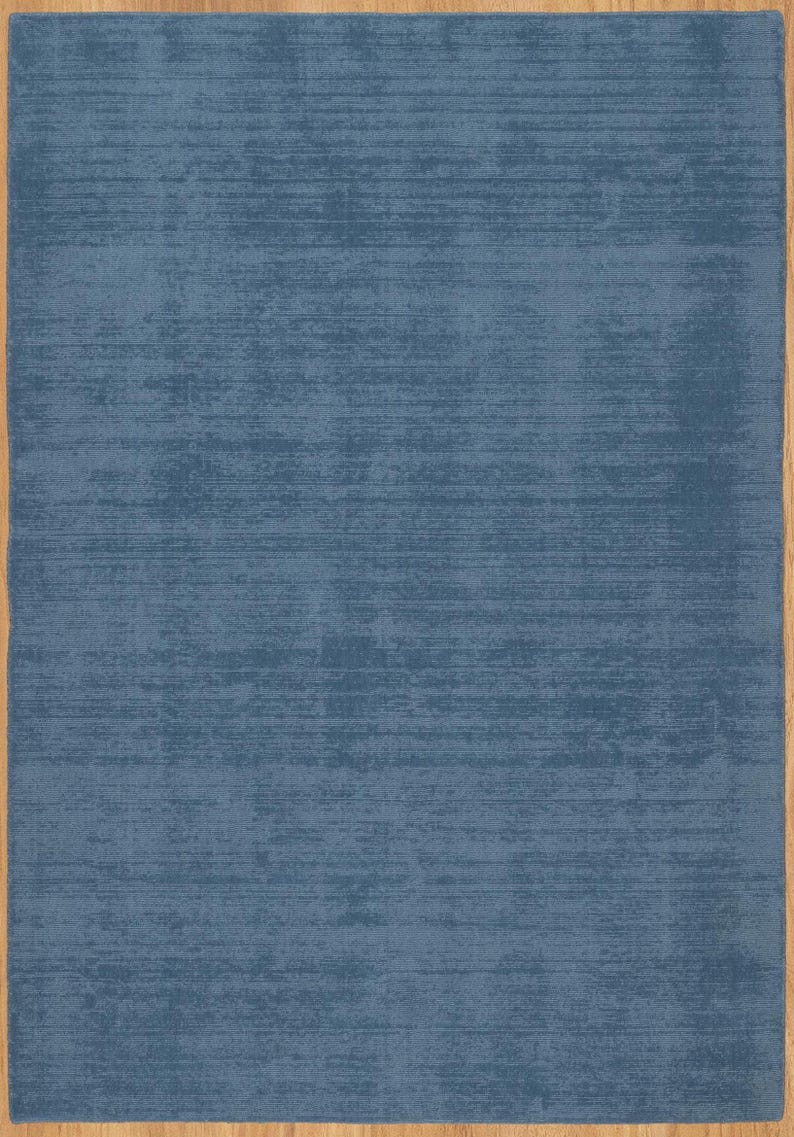May include: A rectangular blue rug with a textured surface. The rug has a solid blue color with a lighter, distressed effect. The rug is framed by a thin, light brown border, creating a clean, modern look.
