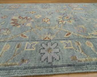 May include: A close-up of a light blue rug with a floral pattern. The rug has a subtle sheen and a soft texture.