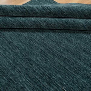 May include: A folded section of teal-colored fabric with a textured, diagonal pattern. The fabric appears to be thick and soft, with visible folds and shadows. The material is a solid teal color, with a subtle sheen.