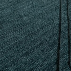 May include: A teal-colored rug with a textured, diagonal pattern. The rug is partially rolled up, revealing the underside and a glimpse of the wooden floor. The fabric has a soft, plush appearance.