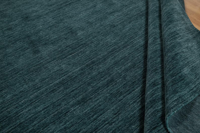 May include: A teal-colored rug with a textured, diagonal pattern. The rug is partially rolled up, revealing the underside and a glimpse of the wooden floor. The fabric has a soft, plush appearance.