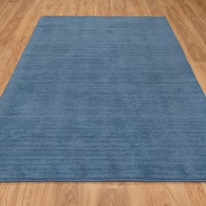 May include: A rectangular, solid blue rug with a textured surface. The rug is placed on a wooden floor, creating a contrast in color and texture. The rug's dimensions are not visible.