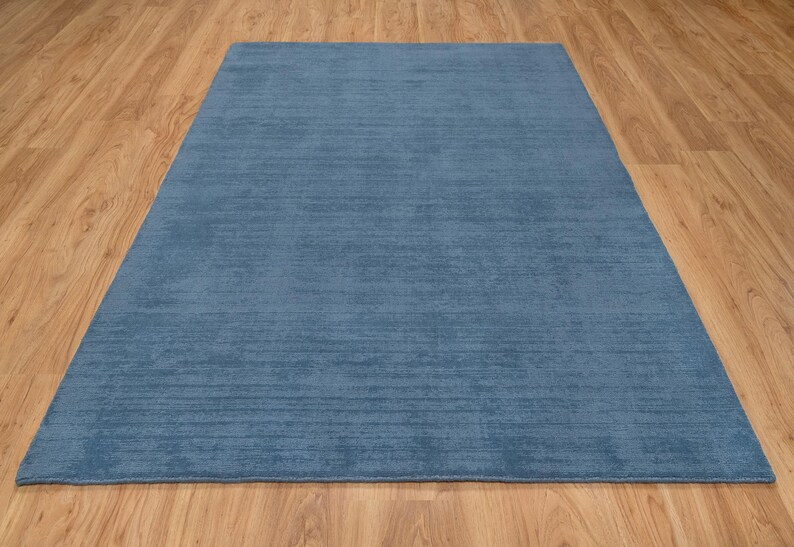 May include: A rectangular, solid blue rug with a textured surface. The rug is placed on a wooden floor, creating a contrast in color and texture. The rug's dimensions are not visible.