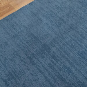 May include: A section of a blue rug with a textured surface. The rug has a diagonal pattern and is adjacent to a section of light brown wooden flooring.