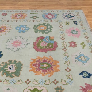 May include: A light green rug with a repeating pattern of colorful floral designs. The rug has a subtle distressed look and a fringed edge.