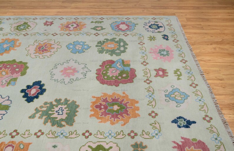 May include: A light green rug with a repeating pattern of colorful floral designs. The rug has a subtle distressed look and a fringed edge.