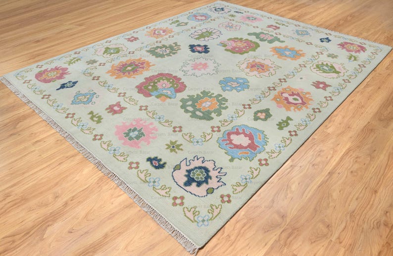 light green oushak rug by carpet bazaar with baby pink, coral, blue, green and orange abstract floral pattern.