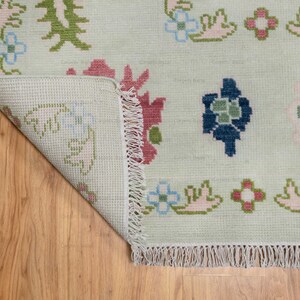 May include: A white rug with a floral pattern in shades of pink, blue, green, and brown. The rug has a fringe border.