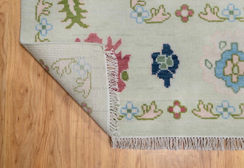 May include: A white rug with a floral pattern in shades of pink, blue, green, and brown. The rug has a fringe border.
