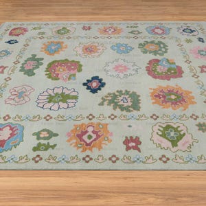 May include: A light blue rug with a floral pattern in shades of pink, green, blue, and orange. The rug has a border of small flowers and leaves.