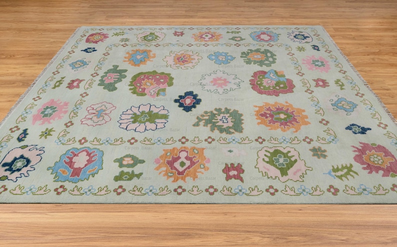 May include: A light blue rug with a floral pattern in shades of pink, green, blue, and orange. The rug has a border of small flowers and leaves.