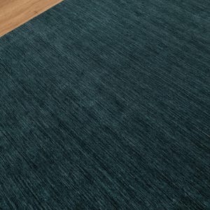 May include: A close-up shot of a teal-colored rug with a textured surface. The rug has a diagonal pattern and is paired with a section of light brown wood. The rug's color is a deep, saturated teal.
