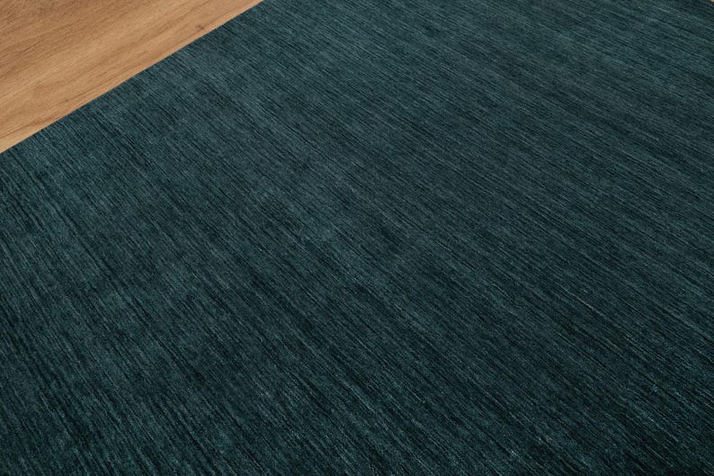 May include: A close-up shot of a teal-colored rug with a textured surface. The rug has a diagonal pattern and is paired with a section of light brown wood. The rug's color is a deep, saturated teal.