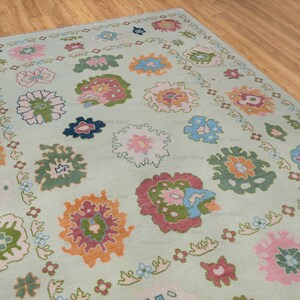 May include: A light green rug with a floral pattern. The rug features a variety of colors, including pink, blue, orange, and green. The flowers are arranged in a symmetrical pattern.
