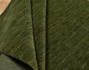Pode incluir: Um tapete verde-oliva dobrado, revelando sua textura e construção. As fibras apresentam um padrão diagonal sutil. A parte inferior é de um tom de verde mais escuro. O tapete tem um tom rico e terroso.
