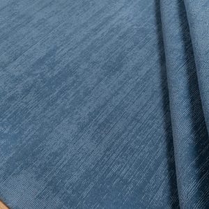 May include: A close-up of a blue rug with a textured surface. The rug has a soft, plush appearance and is folded over, revealing the underside. The color is a muted, medium blue.